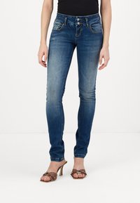 Jeans ajustados de denim azul con un lavado medio, que presentan un diseño de cinco bolsillos, cierre frontal de dos botones y un ligero desgaste sutil.