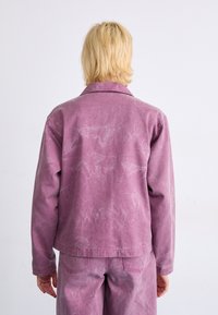 Lys lilla denimjakke med krage, lange ermer og en lett slitt tekstur. Båret med matchende lys lilla bukser.