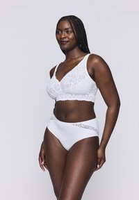 Bralette bianco in pizzo con design a V e spalline regolabili, abbinato a mutandine bianche a vita alta con dettagli in pizzo lungo la vita.