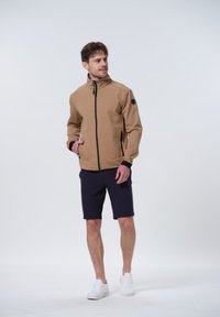 Chaqueta beige con cremallera y cuello alto, con acentos negros, combinada con pantalones cortos azul marino. Corte clásico, textura suave y bolsillos laterales.