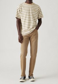 T-shirt rayée beige et blanche avec un col rond et le logo Levi's, associée à un pantalon beige droit et des baskets noires.