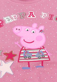 Pink cotton t-shirt featuring a cartoon pig wearing a striped dress and roller skates. Background has white polka dots and colorful stars.