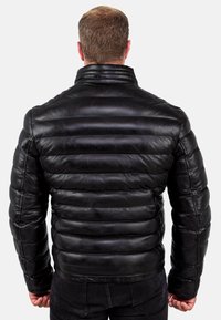 Giubbotto in pelle nera con imbottitura, cuciture orizzontali, colletto alto e superficie testurizzata. Caratterizzato da un design aderente e una leggera lucentezza.