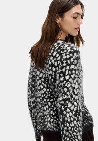 Schwarzer und weißer gemusterter Pullover mit einer flauschigen Textur, lockerer Passform und rundem Ausschnitt. Akzente umfassen ein auffälliges, gesprenkeltes Design.