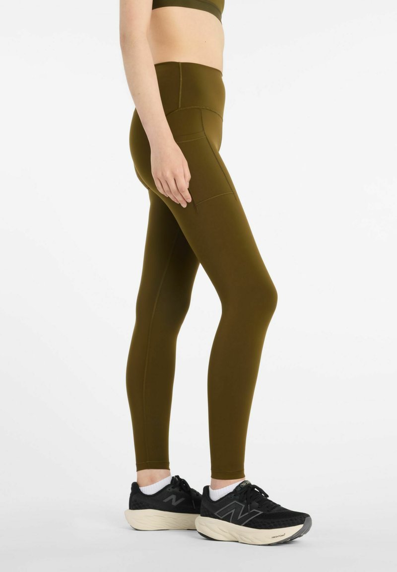 Olivgröna leggings i stretchigt tyg med hög midja och sidfickor, matchade med svarta träningsskor.