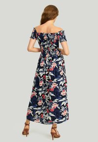 Robe maxi avec imprimé floral marine, design décolleté, buste élastique et taille smockée, présentant des manches courtes et une jupe fluide.