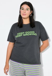 Czarnoszary,oversizowy t-shirt z zielonym napisem "KEEP GOING KEEP GROWING". Miękka tkanina, luźny krój, okrągły dekolt i krótkie rękawy.