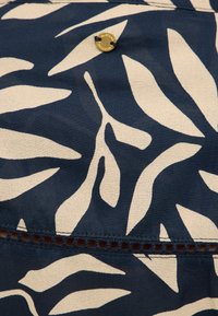 Tissu bleu marine avec des motifs de feuilles ivoire, ornée d'un bouton doré décoratif et d'un détail de couture complexe le long de l'ourlet.