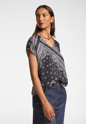 Blusa a maniche corte, bianca e nera, con scollo a V e tessuto leggero; presenta motivi paisley e floreali. Abbinata a jeans.