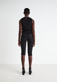 Black sleeveless top paired with black fitted bike shorts, both showcasing a smooth texture. High-heeled sandals complete the outfit.