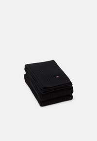 Écharpe noire côtelée pliée avec un petit logo brodé comportant des accents rouges, blancs et bleus. Texture douce, forme rectangulaire.