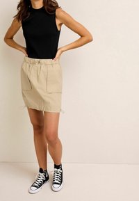 Débardeur noir côtelé, jupe beige avec cordon de serrage et deux poches avant, baskets montantes noires. Tissu lisse, coupe décontractée et design casual.