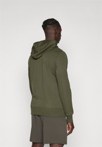 Felpa verde oliva con cappuccio regolabile, maniche lunghe e polsini a coste, abbinata a pantaloni shorts dello stesso colore. Tessuto morbido, design minimalista.