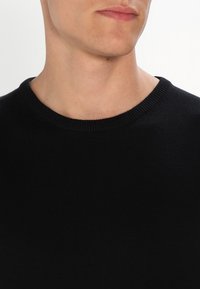 Zwart gebreid sweater met een ronde hals en geribbelde onderkant. Heeft een gladde textuur zonder zichtbare patronen of hardwaredetails.