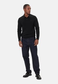 Maglione polo nero a maniche lunghe con collo a polo e logo discreto; abbinato a jeans blu scuro e scarpe nere con lacci.