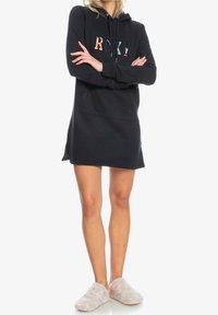 Robe sweat à capuche noire avec une poche kangourou et un logo "ROXY" coloré sur la poitrine. Texturé doux, longueur mi-cuisse, coupe décontractée.