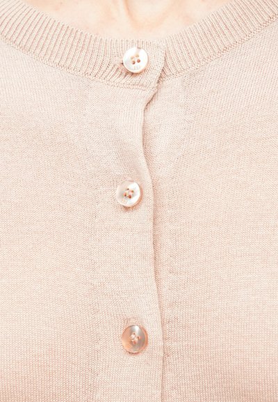 Hellrosa gestrickte Strickjacke mit drei glänzenden, runden Knöpfen, die vorne in der Mitte geschlossen sind, Nahaufnahme des Halsausschnitts und des oberen Brustbereichs.
