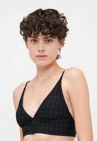 Zwarte driehoekige bralette gemaakt van textuurstof met een geruit patroon, met dunne verstelbare banden en een naadloos ontwerp.