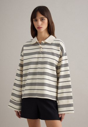 Polo a righe in crema e nero; presenta un colletto, tre bottoni e maniche larghe; realizzato in un tessuto morbido con una finitura strutturata.