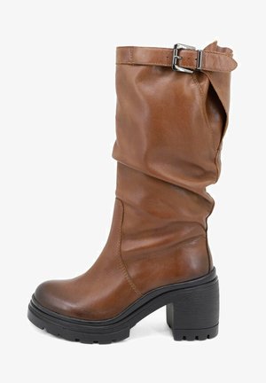 Stivale in pelle marrone alto fino al ginocchio con design a sbalzo, punta rotonda, tacco spesso e nero, e dettagli in metallo vicino alla parte superiore.