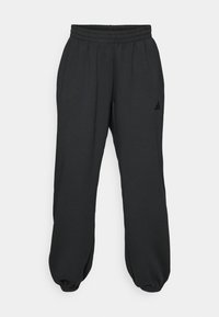 Svarte joggebukser laget av myk stoff, med elastisk midje, innsnevring nederst på bena, og en liten logo på venstre lår.