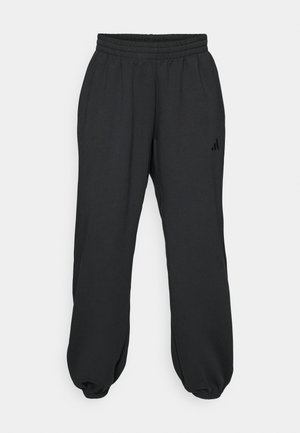 Svarte joggebukser laget av myk stoff, med elastisk midje, innsnevring nederst på bena, og en liten logo på venstre lår.