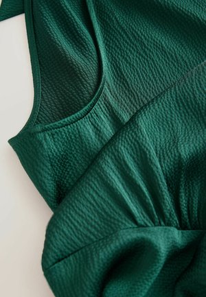 Țesătură verde texturată, cu o secțiune superioară netedă, guler rotund și detalii pliate la margine.