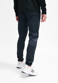 Marineblauwe sportbroek met een aansluitend ontwerp, voorzien van een gladde textuur, zijzakken en een subtiele logodetail, gecombineerd met witte sneakers.