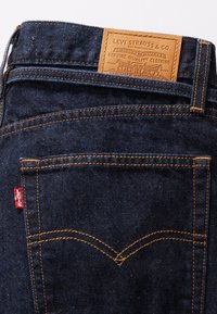 Poche arrière d'un jean Levi's bleu foncé avec des coutures orange et un patch en cuir beige Levi Strauss & Co. à la taille.