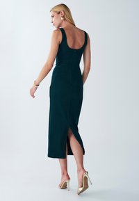 Tyrkysové šatky bez rukávov s výstrihom na chrbte, priliehavý strih a bočný rozparok, v kombinácii so zlatými lodičkami na vysokom podpätku. Hladká, elegantná tkanina.
