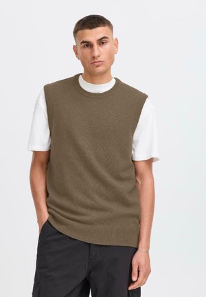 Brown knitted sleeveless sweater over a white t-shirt, featuring a round neck and ribbed edges, with a relaxed fit and smooth texture.