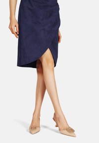 Gonna avvolgente in finta pelle scamosciata blu navy con uno spacco alto, abbinata a décolleté beige a punta con tacco slingback, caratterizzate da una fibbia decorativa.