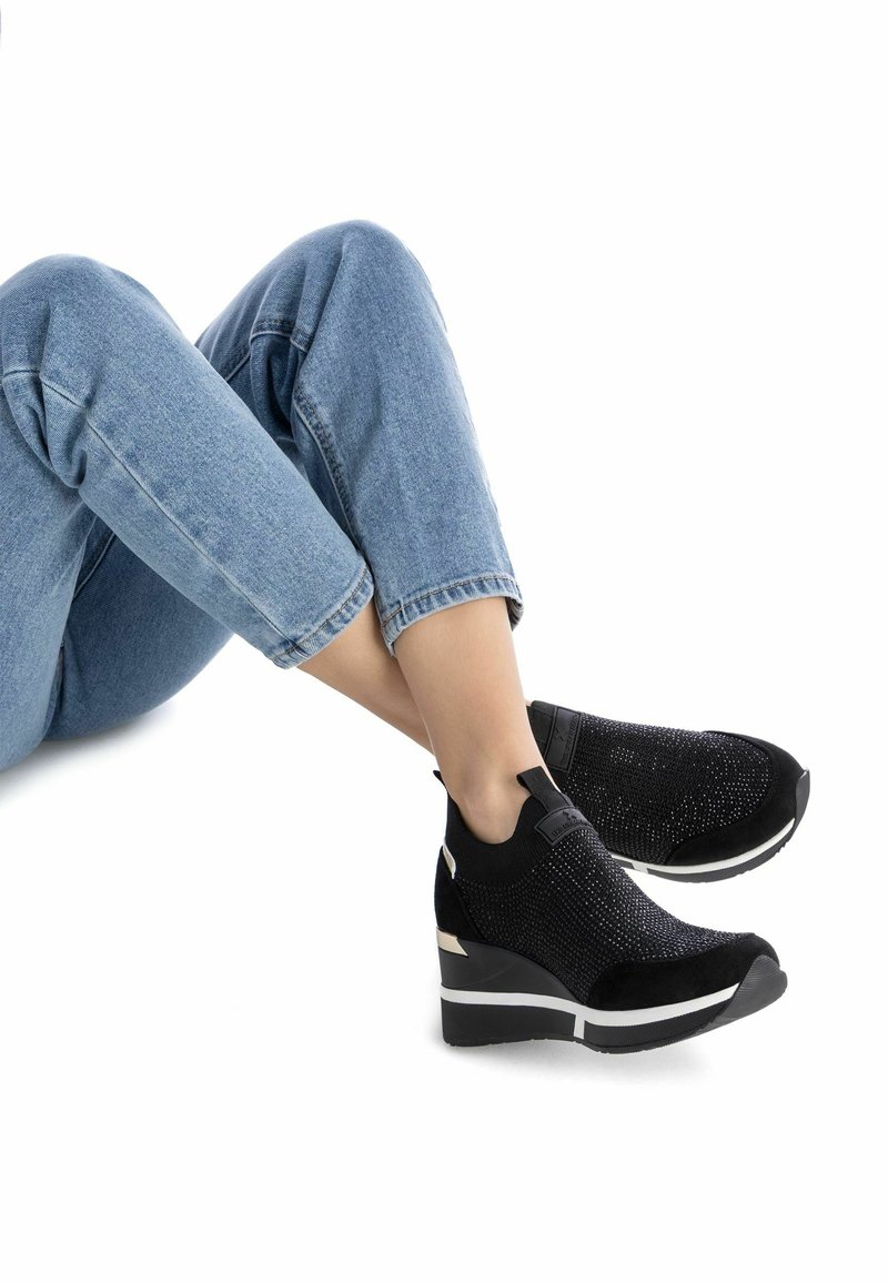 Chaussures à talon noir avec un dessus en tricot texturé, des accents en daim et une semelle intermédiaire blanche. Une languette à l'arrière facilite l'enfilage.