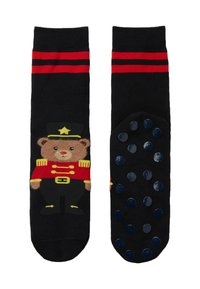 Černé ponožky s medvědem v červené vojenské uniformě, s červenými pruhy na vrchu a gumovými tečkami na podrážce.