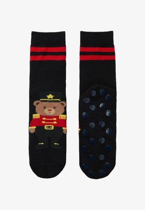 Zwarte sokken met een beer in een rode militaire uniform, met rode strepen aan de bovenkant en rubberen antislip stippen op de zool.