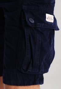 Námorně modré cargo šortky s kapsou na knoflík a bílou cedulkou s nápisem "Superdry Japan Spirit British Design."