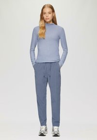 Lichtblauw langwerpig shirt met een hoge hals, gecombineerd met losse, lichtblauwe broek en zilveren sportschoenen, met elastische tailleband en zakken.