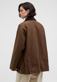 Brown oversized jacket with a corduroy collar, snap buttons, and side vents. Smooth fabric, relaxed fit. Back view displayed.