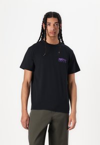 Zwarte katoenen t-shirt met een paarse grafische print op de linkerborst. Korte mouwen en een ronde hals.