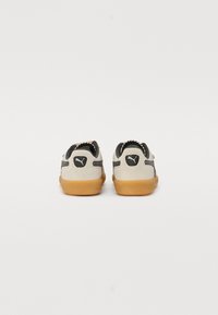 Sneakers Puma w jasnym beżu z czarnymi akcentami, z teksturowanym wierzchem i podeszwą z gumy. Szczegółowe logo z tyłu i z boku.