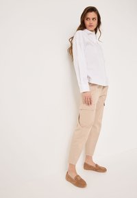 Vit skjorta med knappar, beige cargo byxor med fickor och bruna loafers. Måttliga texturer och neutrala färger skapar en enkel outfit.