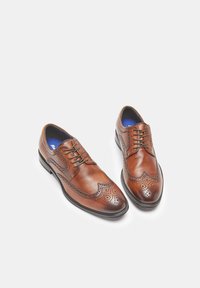 Smeđe kožne brogue cipele s dekorativnim perforacijama, svezanjem, zaobljenim vrhom i plavim ulošcima. Glatka tekstura i elegantna silueta.