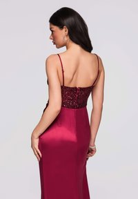 Robe de soirée bordeaux avec un corsage orné de sequins et une jupe en satin. Bretelles spaghetti et silhouette cintrée mettent en valeur le design.