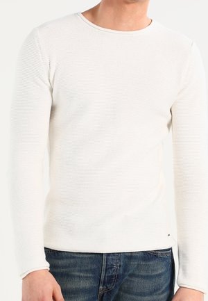 Weißer Langarmpullover mit strukturiertem Strickmuster, Rundhalsausschnitt und gerippten Bündchen, kombiniert mit blauen Jeans.