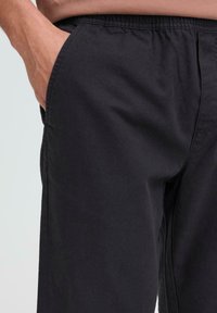 Schwarze, leichte Stoffhosen mit elastischem Bund und Seitentaschen, die eine glatte Textur und eine entspannte Passform zeigen.