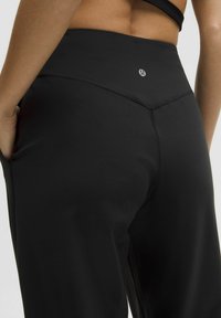 Hoch taillierte schwarze Sportleggings aus glattem Stoff, mit einem dezenten Logo und sauberer Naht, sowie Taschen auf beiden Seiten.