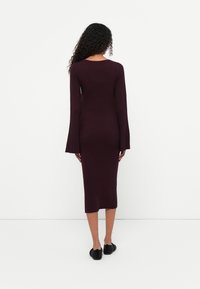 Abito midi lavorato a maglia in un profondo bordeaux con una texture a costine e maniche lunghe svasate, caratterizzato da un collo rotondo e una silhouette aderente.