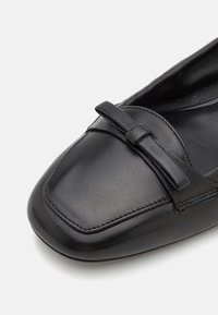 Zwarte leren platte schoen met een vierkante teen, voorzien van een decoratieve strikaccent en subtiele textuur. Het interieur is glad en ongewd.