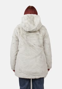 Giacca in ecopelliccia grigio chiaro con cappuccio, caratterizzata da una superficie morbida e testurizzata e una vestibilità leggermente oversize, che arriva a metà coscia.