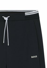 Mörkblå joggingbyxor i mjukt material, med en vit dragsko och randig midja, och en "BOSS"-logotyp i en kontrasterande ljus färg.